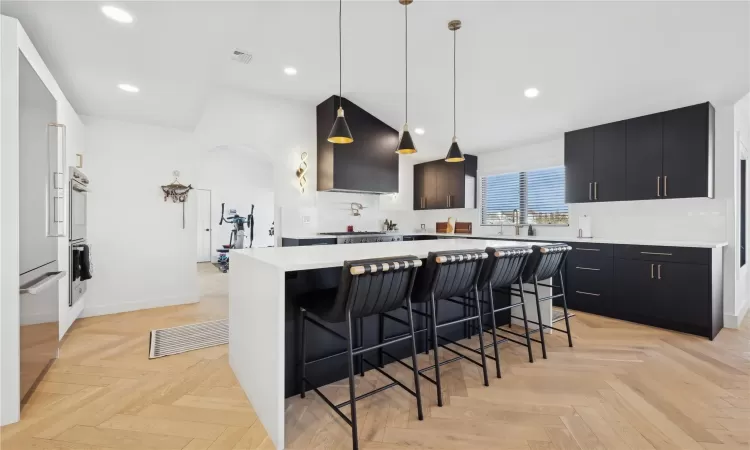 Kitchen featuring a breakfast bar area, light parquet flooring, hanging light fixtures, a center island, and sink