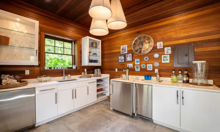 Kitchen with white cabinets, wooden walls, wood ceiling, and sink