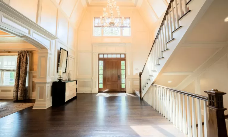 Foyer entrance featuring a high ceiling, ornamental molding, a notable chandelier, and dark wood-type flooring