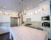 Kitchen with stainless steel appliances, white cabinets, hanging light fixtures, and light stone countertops