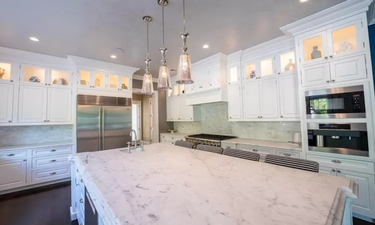 Kitchen with stainless steel appliances, white cabinets, hanging light fixtures, and light stone countertops