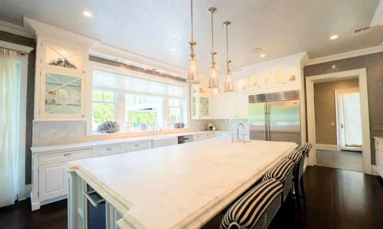 Kitchen with stainless steel built in refrigerator, a center island with sink, white cabinets, and pendant lighting