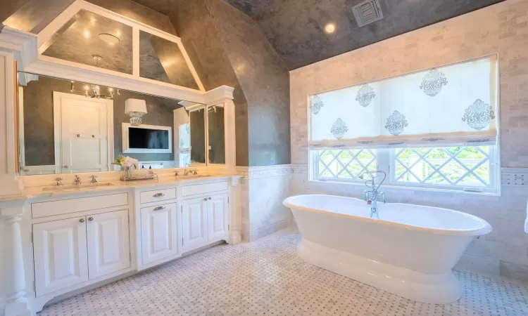 Bathroom with tile walls, high vaulted ceiling, vanity, and a bathing tub