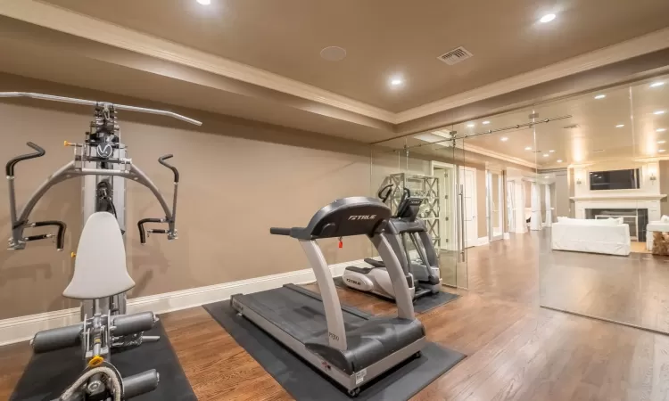 Exercise room featuring ornamental molding, a fireplace, and hardwood / wood-style flooring