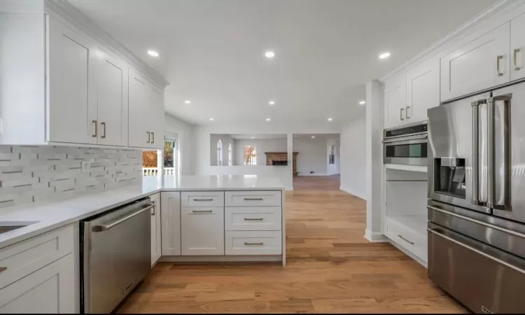 Kitchen with white cabinets, light hardwood / wood-style floors, kitchen peninsula, backsplash, and appliances with stainless steel finishes