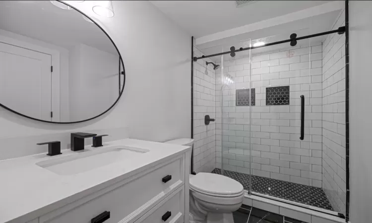 Bathroom featuring toilet, tile patterned flooring, a shower with shower door, and vanity