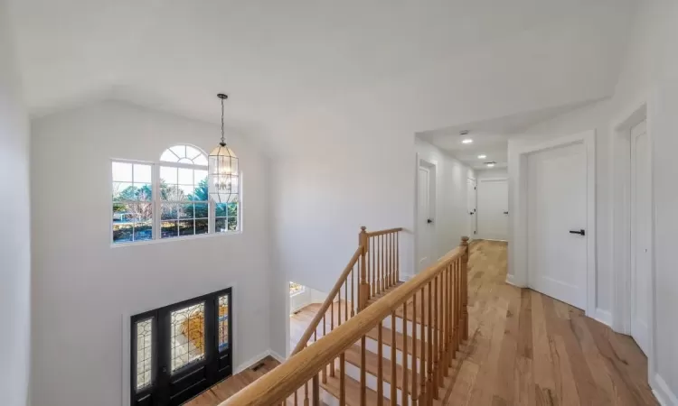 Hallway featuring lofted ceiling, an inviting chandelier, and light wood-type flooring