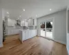 Kitchen featuring kitchen peninsula, wall chimney exhaust hood, light wood-type flooring, white cabinetry, and high quality fridge