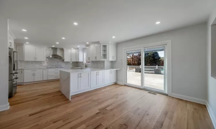 Kitchen featuring kitchen peninsula, wall chimney exhaust hood, light wood-type flooring, white cabinetry, and high quality fridge