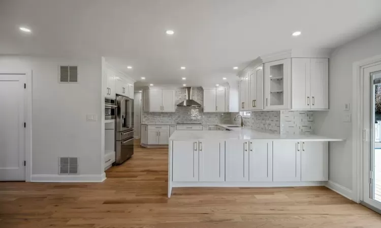 Kitchen featuring white cabinetry, kitchen peninsula, sink, light hardwood / wood-style flooring, and wall chimney range hood