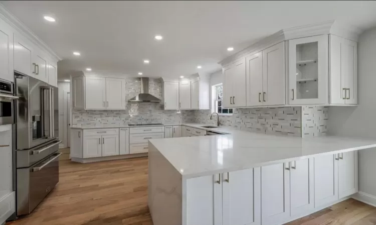 Kitchen featuring kitchen peninsula, wall chimney range hood, light hardwood / wood-style floors, white cabinetry, and sink