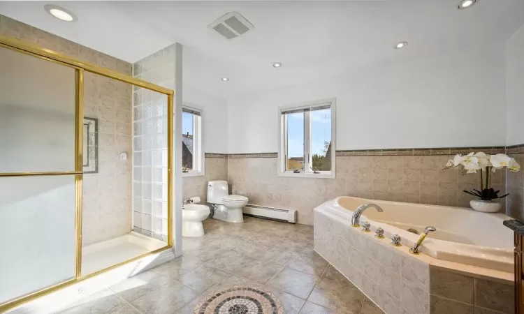 Bathroom with toilet, a bidet, tile walls, a baseboard heating unit, and independent shower and bath