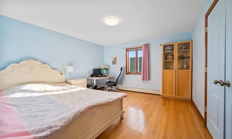 Bedroom with light wood-type flooring and a baseboard heating unit