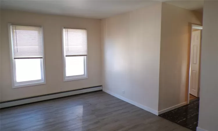 Empty room featuring baseboard heating and dark wood-type flooring