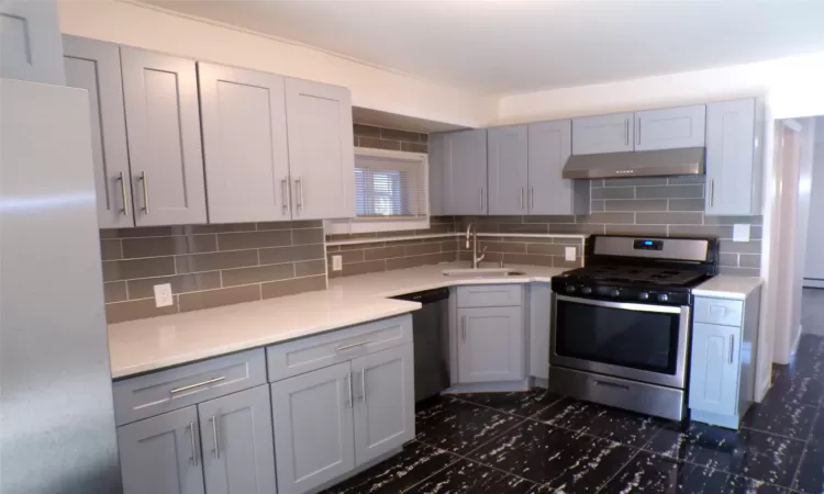 Kitchen with appliances with stainless steel finishes, gray cabinets, backsplash, and sink