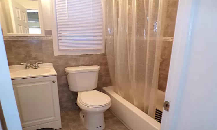 Full bathroom with toilet, shower / bathtub combination with curtain, tile walls, and vanity