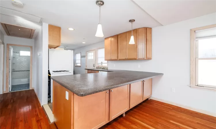 Kitchen featuring white appliances, kitchen peninsula, dark hardwood / wood-style floors, hanging light fixtures, and sink