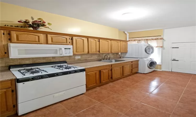 Kitchen with sink, white appliances, decorative backsplash, light tile patterned floors, and stacked washer and clothes dryer