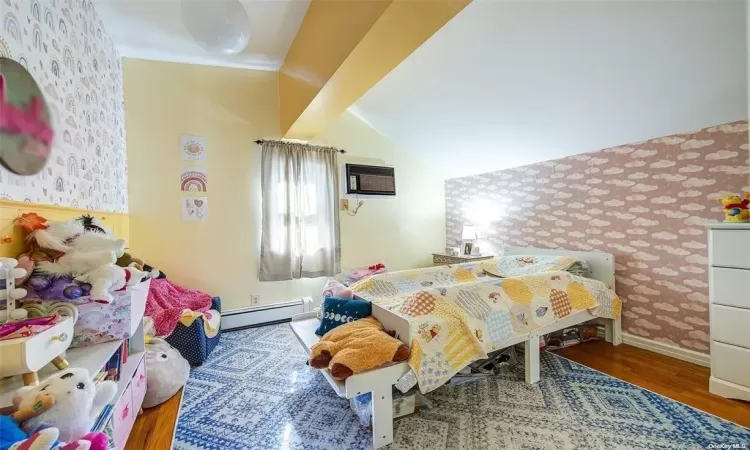 Bedroom with a wall mounted air conditioner, vaulted ceiling, a baseboard radiator, and hardwood / wood-style flooring