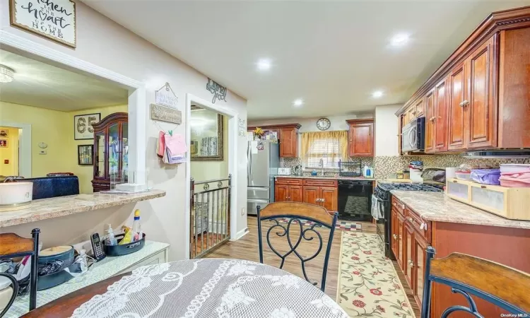 Kitchen featuring backsplash, light wood-type flooring, black appliances, and light stone counters