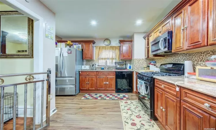 Kitchen with light stone counters, light hardwood / wood-style flooring, black appliances, tasteful backsplash, and sink