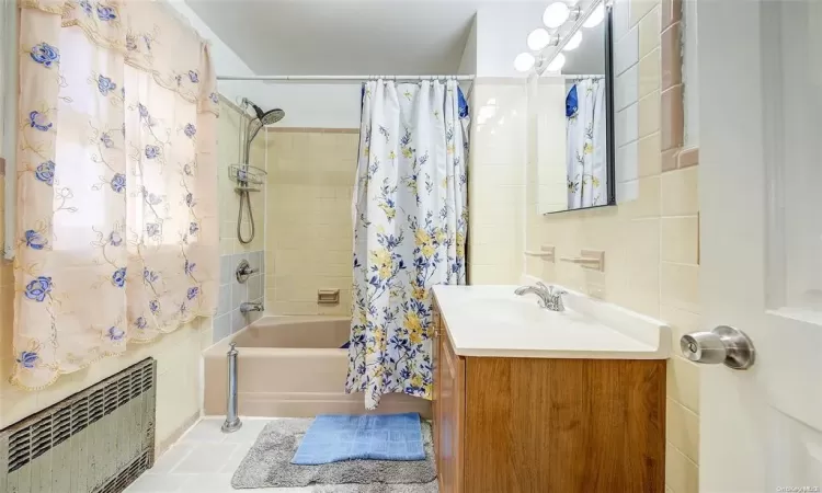 Bathroom with tile walls, tasteful backsplash, radiator, shower / bath combo, and vanity