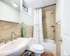 Full bathroom featuring toilet, shower / bath combo with shower curtain, tasteful backsplash, tile walls, and sink