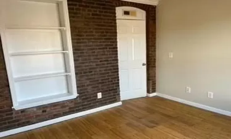 Empty room with brick wall and dark hardwood / wood-style flooring