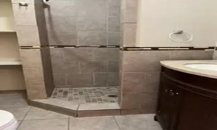 Bathroom with tiled shower, tile walls, toilet, tile patterned floors, and vanity