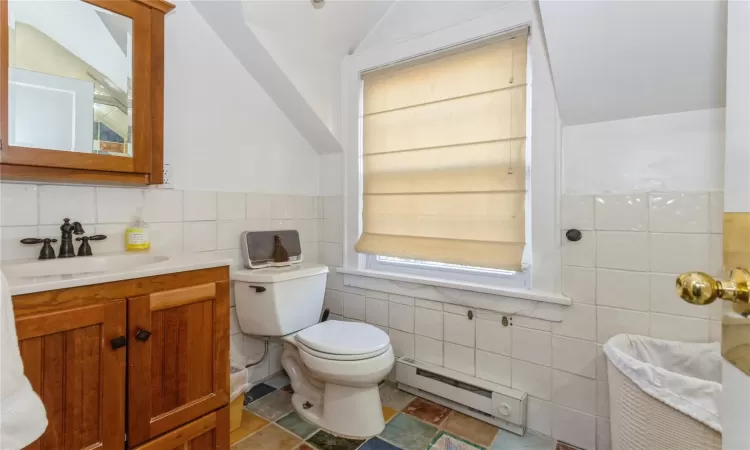 Bathroom featuring toilet, vanity, tile walls, a baseboard heating unit, and lofted ceiling