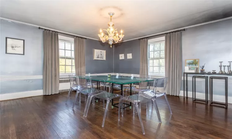 Dining area with dark wood-type flooring, an inviting chandelier, and ornamental molding