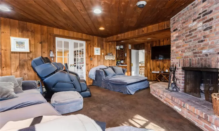 Carpeted living room featuring french doors, a brick fireplace, and wooden walls