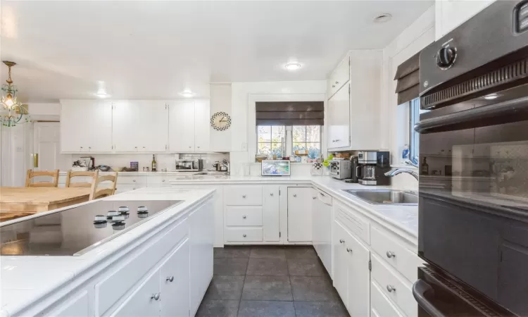 Kitchen featuring sink, white cabinetry, black appliances, and pendant lighting