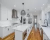 Kitchen with appliances with stainless steel finishes, wall chimney exhaust hood, decorative light fixtures, white cabinetry, and a kitchen island with sink