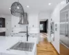 Kitchen with white cabinets, wall chimney exhaust hood, stainless steel appliances, hanging light fixtures, and light hardwood / wood-style flooring