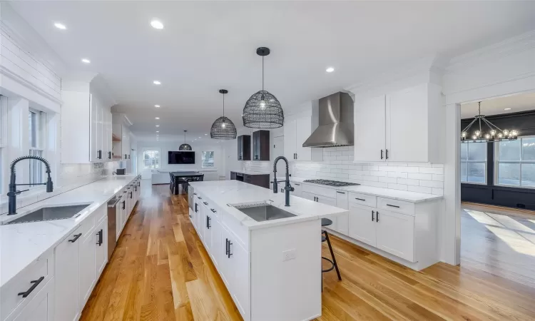 Kitchen featuring gas stovetop, sink, a center island with sink, and wall chimney range hood