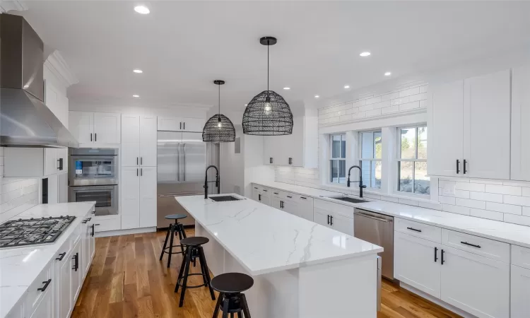 Kitchen with a kitchen island with sink, appliances with stainless steel finishes, wall chimney range hood, and pendant lighting