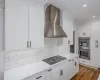 Kitchen with exhaust hood, backsplash, white cabinetry, light stone countertops, and stainless steel appliances