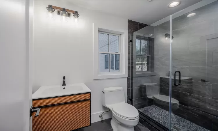 Bathroom featuring toilet, vanity, tile patterned flooring, and a shower with door