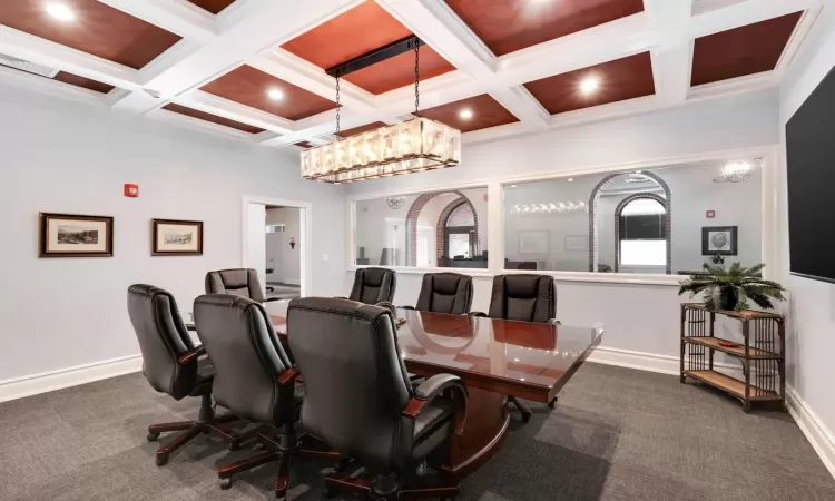 Dining space featuring coffered ceiling, beam ceiling, a notable chandelier, and dark colored carpet