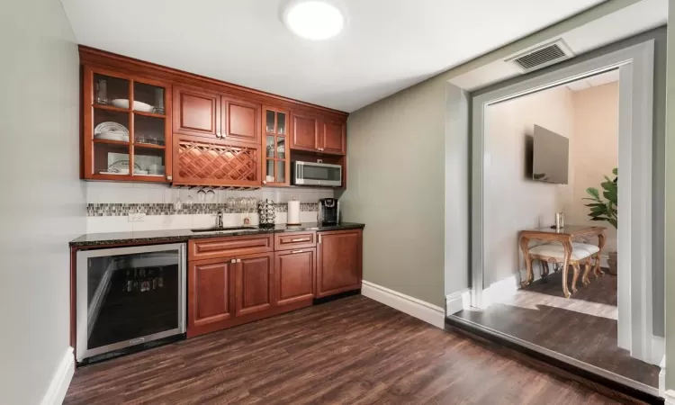 Bar with backsplash, dark hardwood / wood-style floors, dark stone countertops, sink, and beverage cooler