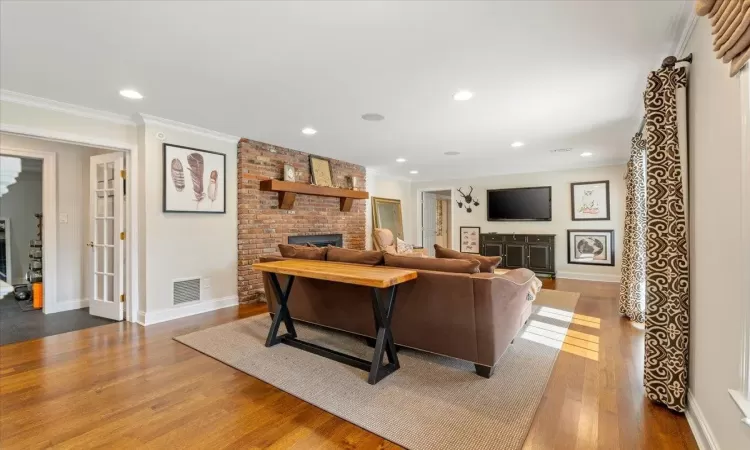 Living room featuring a brick fireplace, hardwood / wood-style floors, and ornamental molding