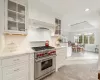 Kitchen with decorative backsplash, white cabinetry, light stone countertops, custom range hood, and luxury stove