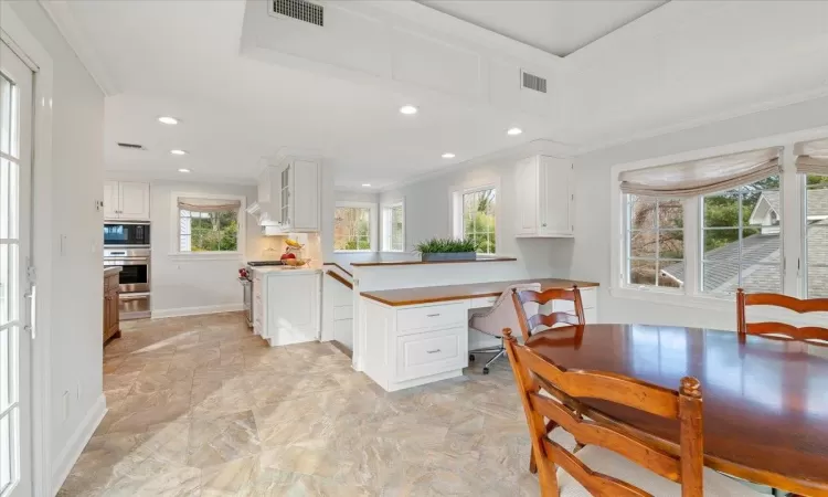 Kitchen with a wealth of natural light, white cabinets, kitchen peninsula, and ornamental molding