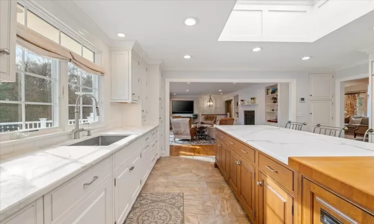 Kitchen featuring ornamental molding, white cabinets, light stone counters, and sink