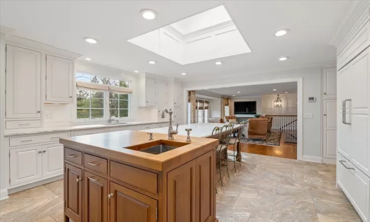 Kitchen featuring white cabinets, a skylight, an island with sink, sink, and crown molding