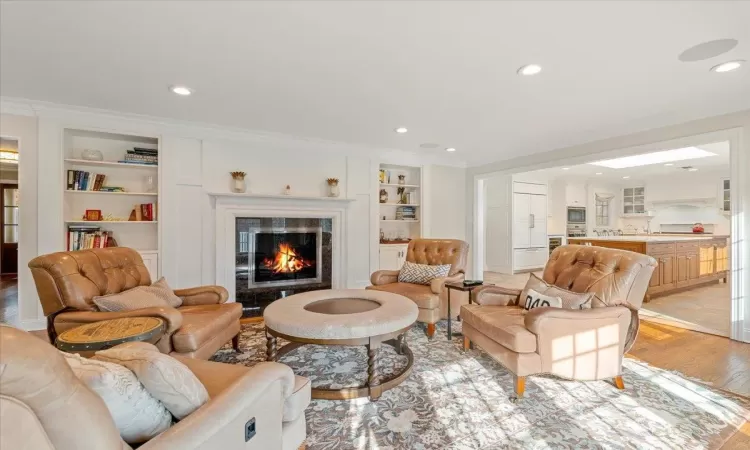 Living room featuring light hardwood / wood-style floors, built in shelves, crown molding, and a fireplace