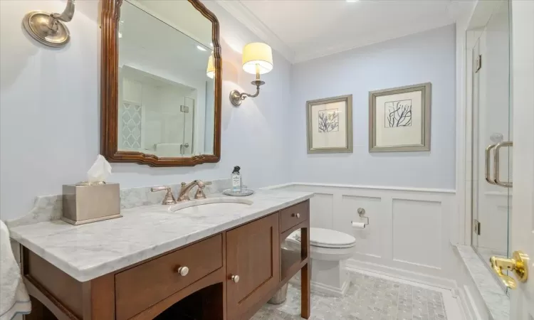 Bathroom featuring an enclosed shower, vanity, toilet, and ornamental molding