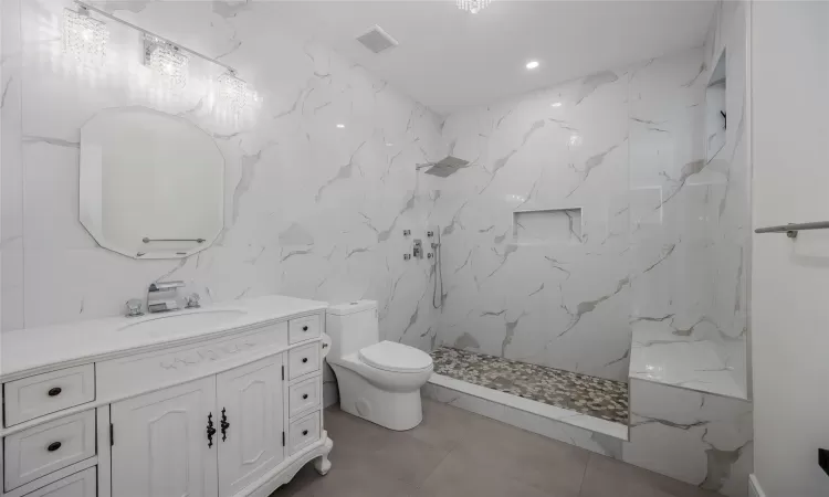 Bathroom with a shower, tile walls, tile patterned flooring, vanity, and toilet