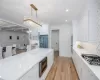 Kitchen featuring appliances with stainless steel finishes, light stone counters, decorative backsplash, white cabinets, and decorative light fixtures